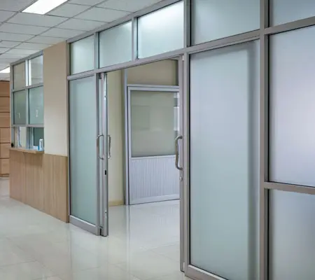 Interior de un edificio donde al centro hay una puerta corrediza enfrentada abierta con herrajes y perfiles de acero inoxidable.