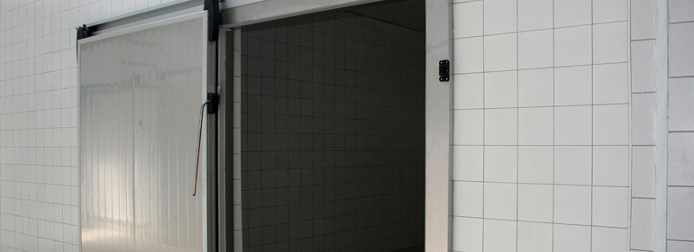 Puerta corrediza de acero inoxidable abierta de un cuarto de refrigeración decorado con azulejo color blanco