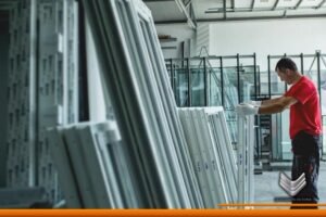 Trabajador con equipo de seguridad en una bodega donde se resguardan distintos materiales para la construcción de puertas de aluminio