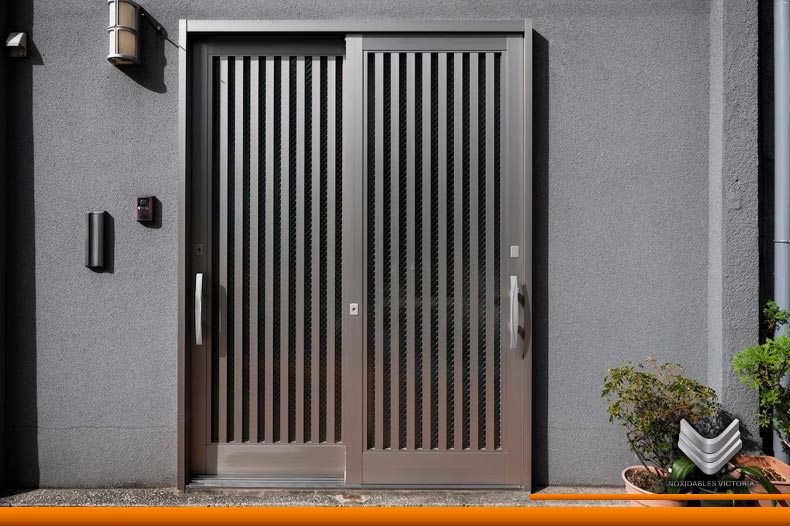 Entrada principal, uno de los tipos de puertas corredizas de acero inoxidable más populares en viviendas, se observa una puerta color gris con decorados en la misma tonalidad y macetas a la derecha