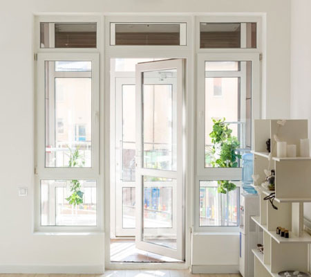 Vista frontal de una ventana color blanco y vidrio, se encuentra en un cuarto que da a un balcón, del lado derecho hay un mueble de madera con varias repisas.