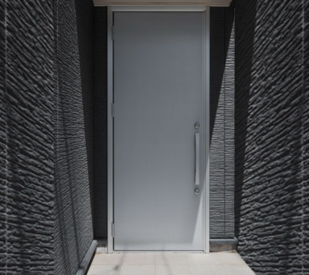 Vista frontal de una puerta para recámara color gris metálico con acabados, la habitación en donde se encuentra tiene acabados grises con una entrada de luz a la derecha