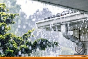 Vista lateral de la esquina de un techo que tiene una canaleta de aluminio mientras está lloviendo, del lado izquierdo se encuentra un árbol