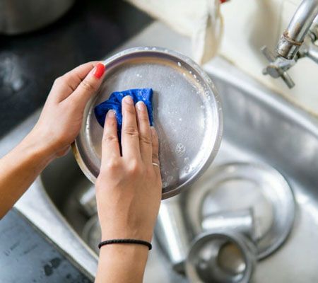 Manos de mujer lavando utensilios de cocina de acero inoxidable en una tarja