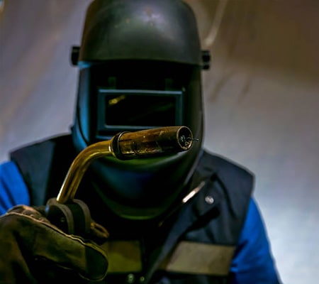Persona con equipo de protección mostrando una antorcha para soldadura MIG